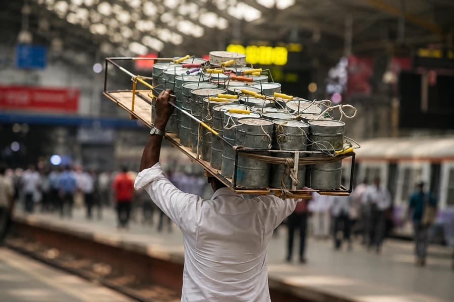 A dabbawala carrying a crate of tiffins along a Mumbai station platform